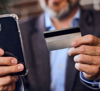 Hombre de mediana edad sujetando su teléfono móvil en una mano y una tarjeta bancaria en la otra